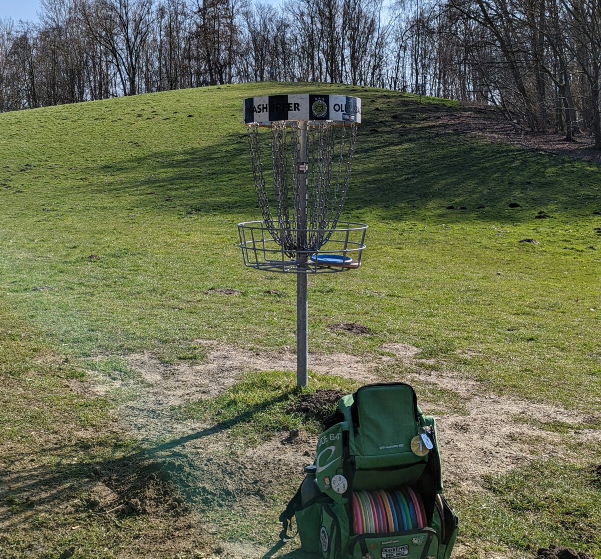 Ein Disc-Golf-Korb im Design der Grashüpfer Olpkebach und ein Disc-Golf-Rucksack